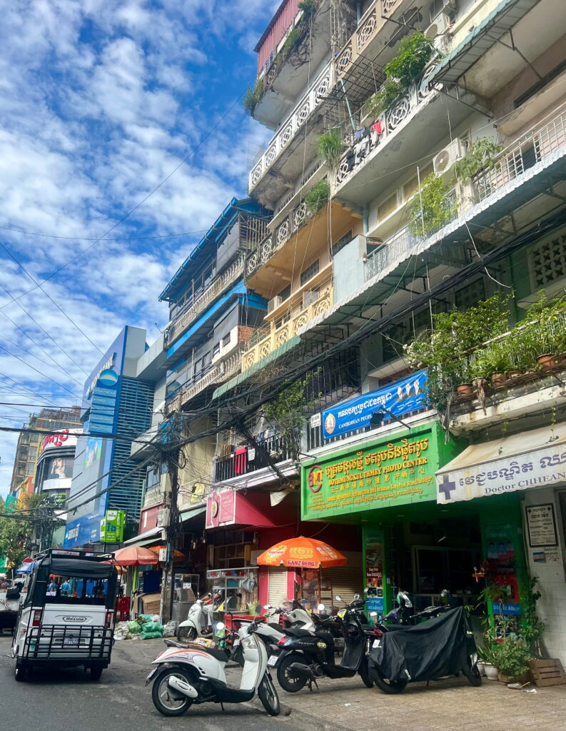 Straßenszene in Phnom Penh mit Tuk Tuk, traditionellen Wohnhäusern und typischen Stromleitungen in Kambodscha
